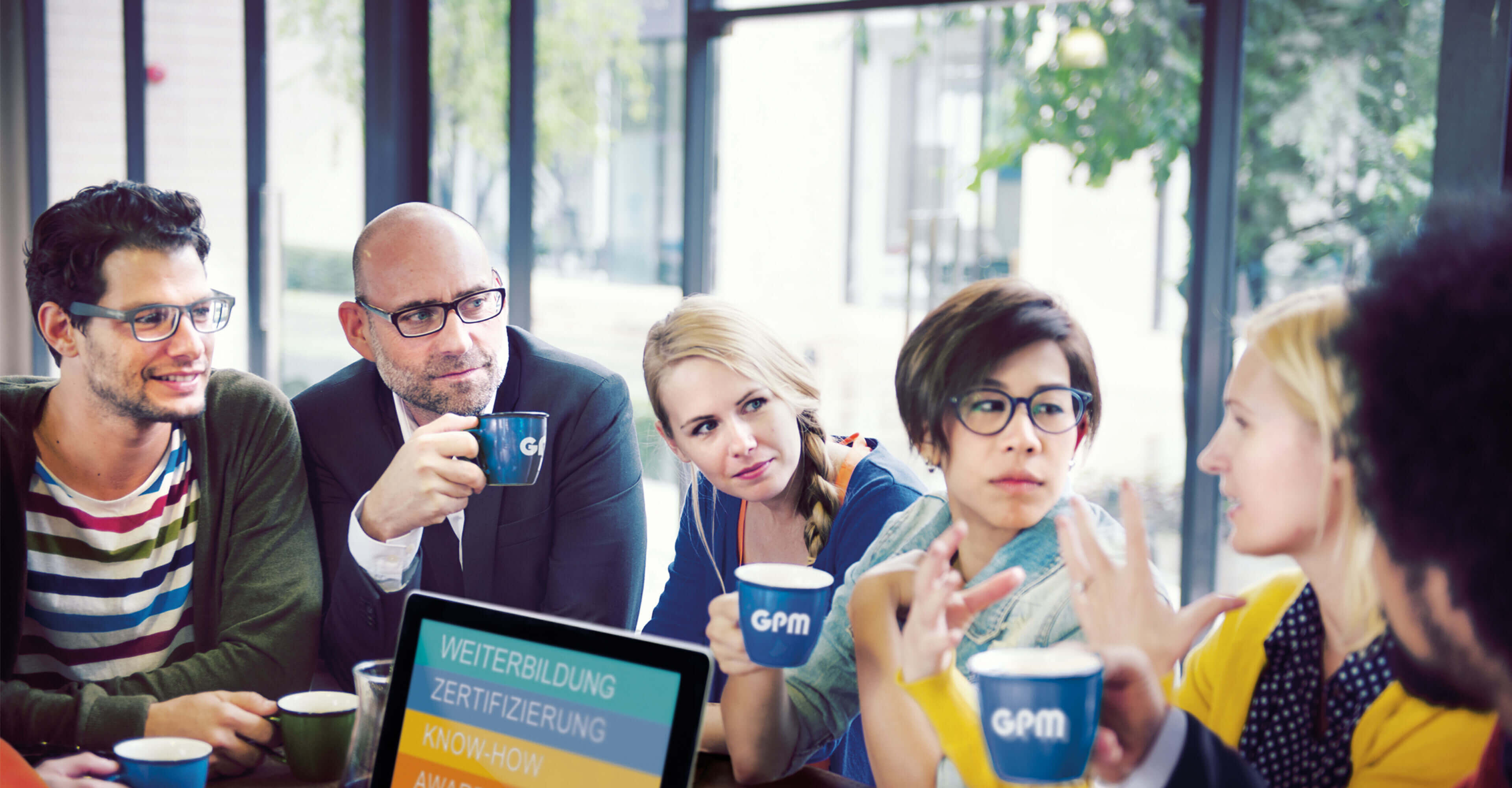 Menschen mit Laptop diskutieren in Arbeitsumgebung und trinken Kaffee aus GPM Tassen