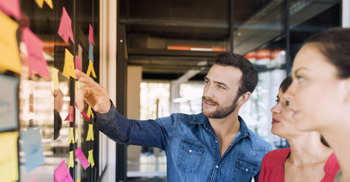 Projektmanagende diskutieren an einer mit Postits beklebten Scheibe